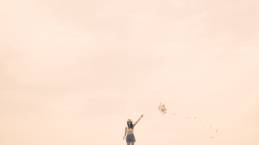 Young woman flying kite on summery day at the beach